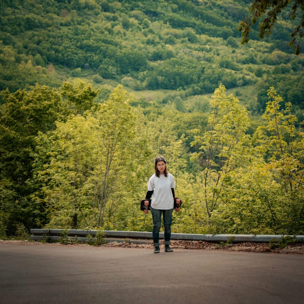 Youthful Skateboarder Standing on Mountain Road With Lush Green Forest Background, Adventure and Outdoor Lifestyle